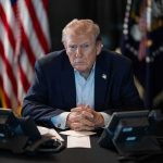 A Trump Catchphrase Gets an Unlikely Revival Donald Trump seated at a table between two desk phones