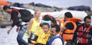 man carries child wearing life jacket at shoreline