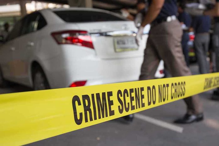 shutterstock_351048443 Yellow crime scene tape in front of a white car with investigators nearby