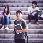 Student holding notebooks on campus steps