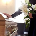 Mourner with lilies beside a wooden casket