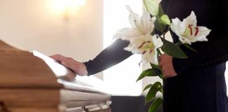 Mourner with lilies beside a wooden casket