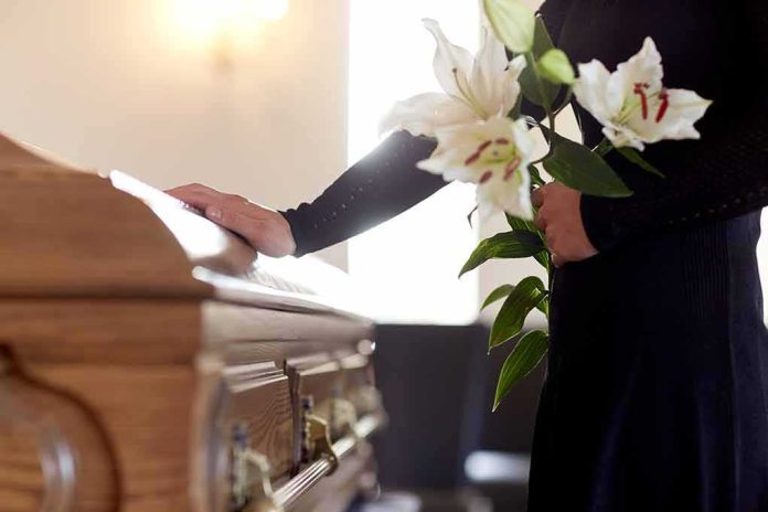 shutterstock_664197991 Mourner with lilies beside a wooden casket